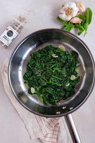Sautéed spinach in a metal pan with garlic and the Salty Provisions Salt + Pepper Blend